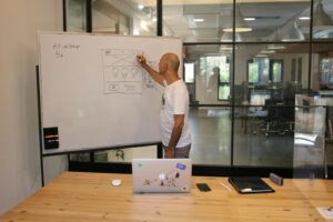 Side view of anonymous hairless male employee in white t shirt drawing draft on whiteboard while working on startup strategy in contemporary office