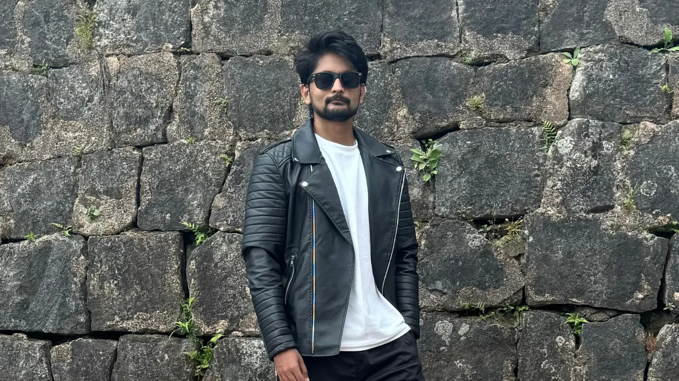 Amar Karthik standing in front of an old fort wall with a cool black jacket