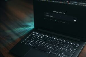 A laptop displays a search bar asking how it can help.